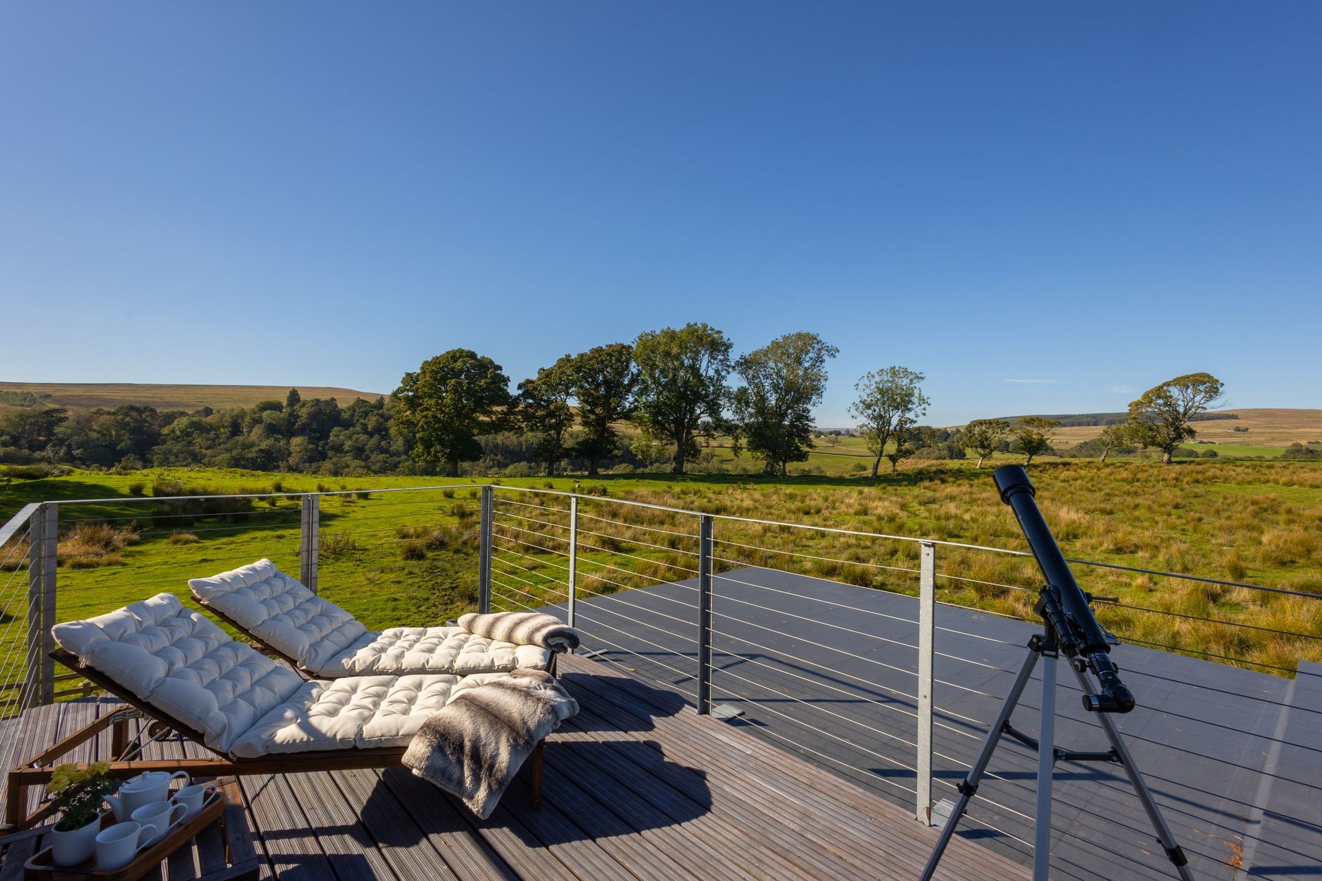 Deck with lounge chair and telescope overlooking a sunny rural landscape under a clear blue sky