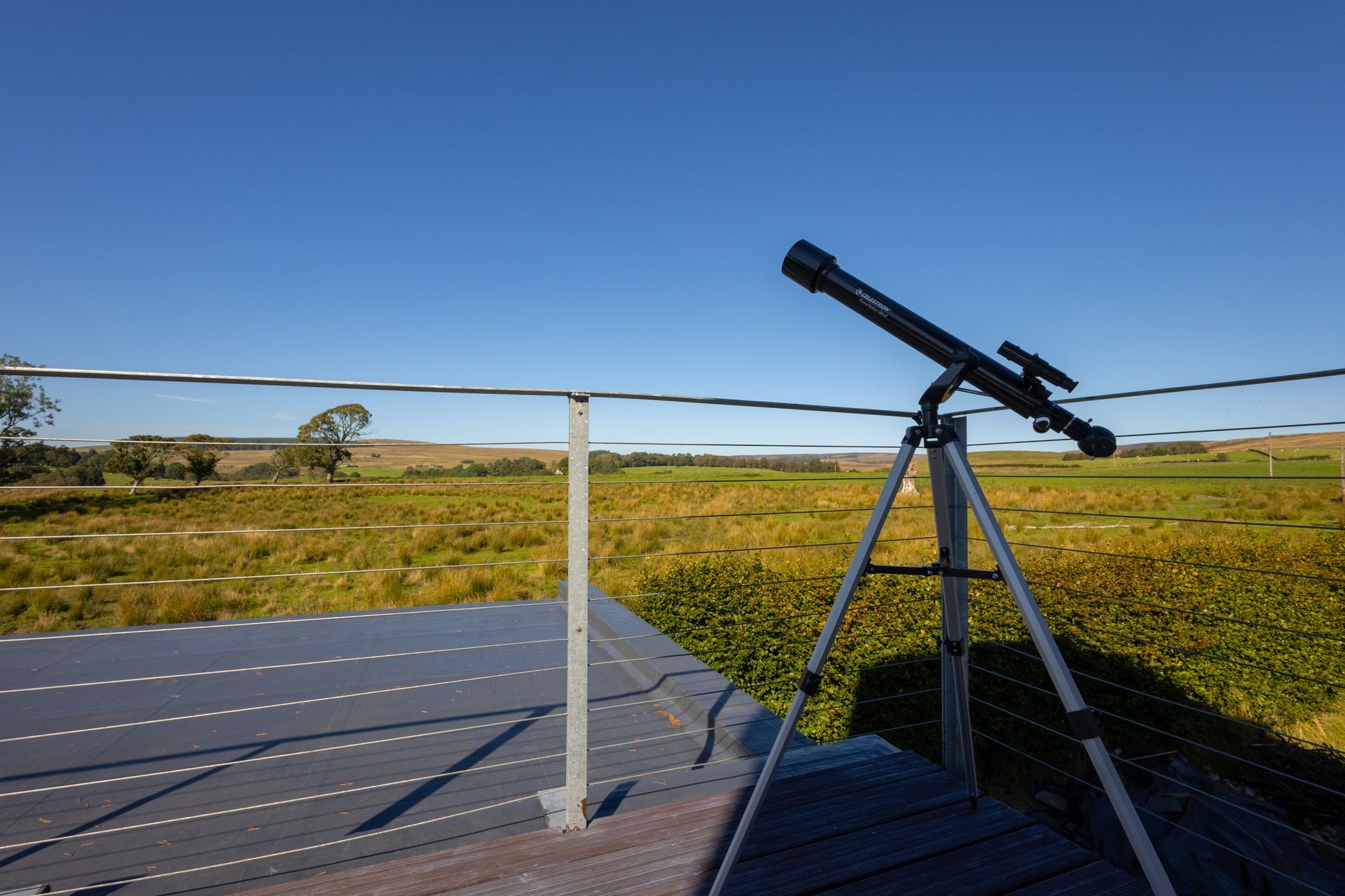 Telescope on a tripod overlooking a grassy field under a clear blue sky.