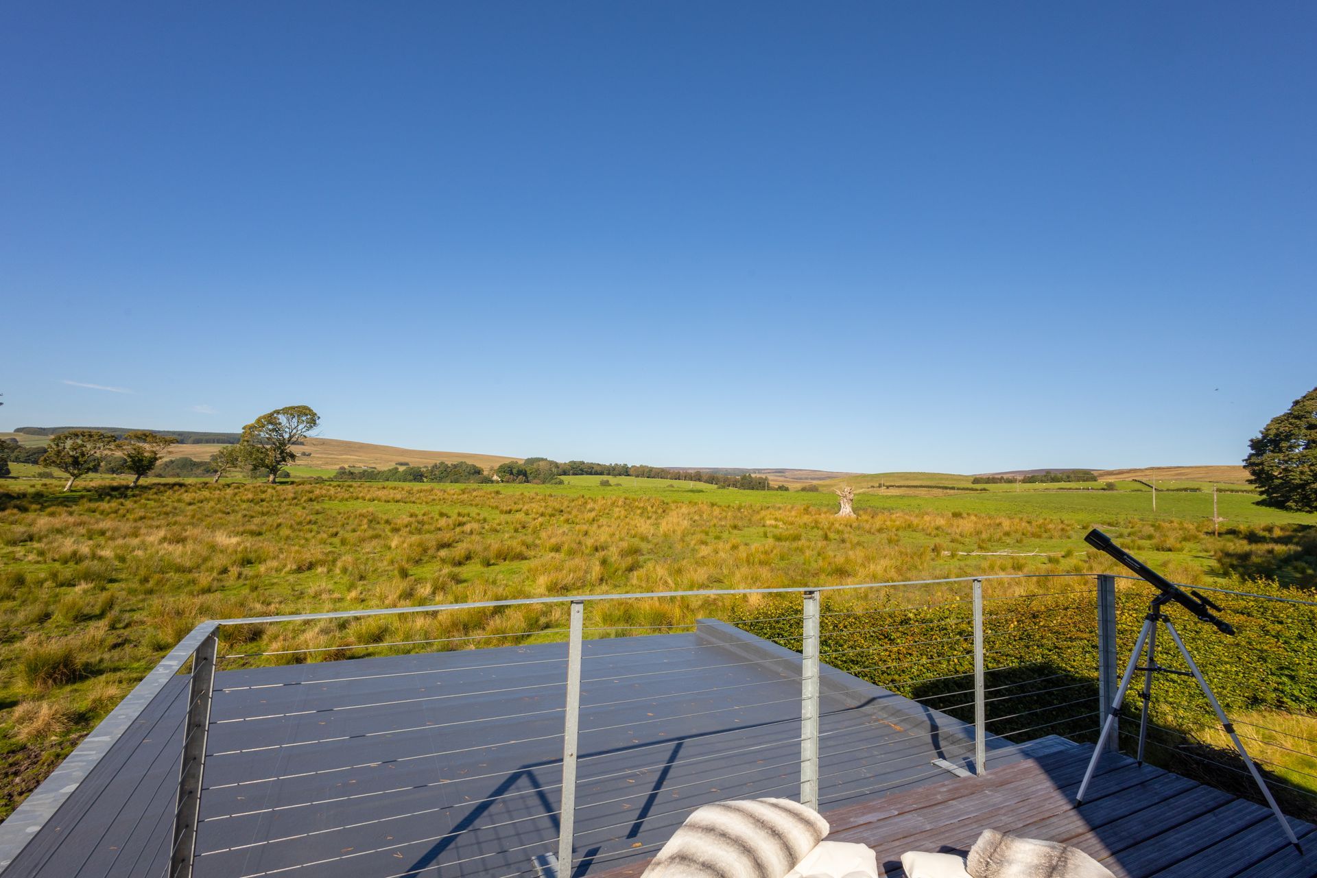Deck overlooking grassy field under a clear blue sky, with white railings in the foreground.