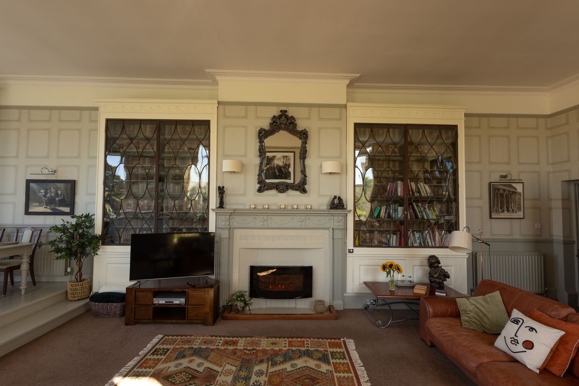 Elegant living room with fireplace, TV, patterned curtains, and brown sofa with orange pillows