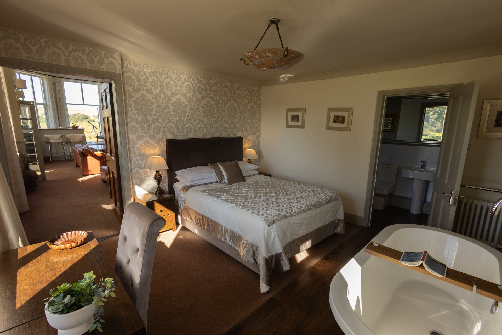 Bright bedroom with a bed, hardwood floors, doorway to a sunlit room, and a small dining table in the foreground