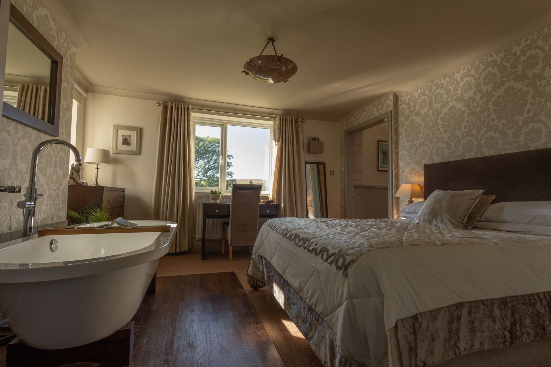 Cozy bedroom with a freestanding bathtub, king bed, window seat, and warm natural light
