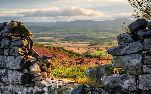 Stone wall opening overlooking a green valley and distant hills under a cloudy sky