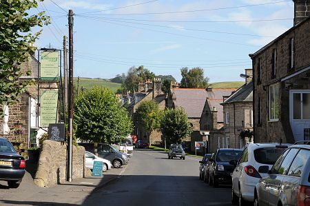 Quiet village street with parked cars, stone houses, and a blue sky. bellingham