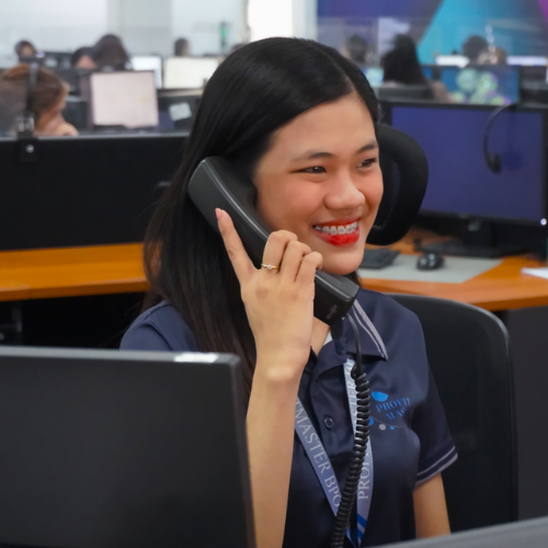 Woman smiling while using a desk phone in a busy office call center