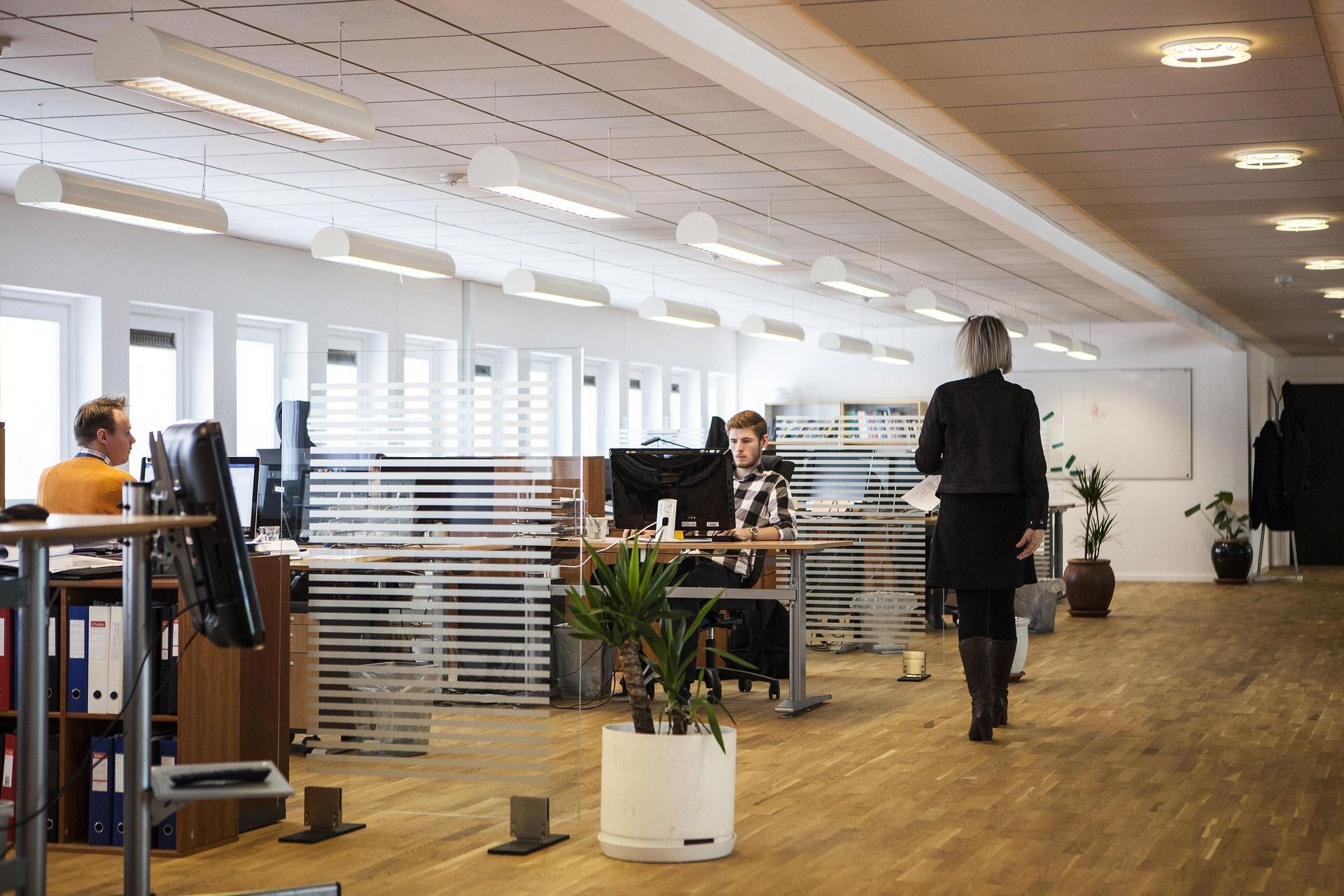 Modern office interior with people at desks, glass partitions, and a person walking across the room