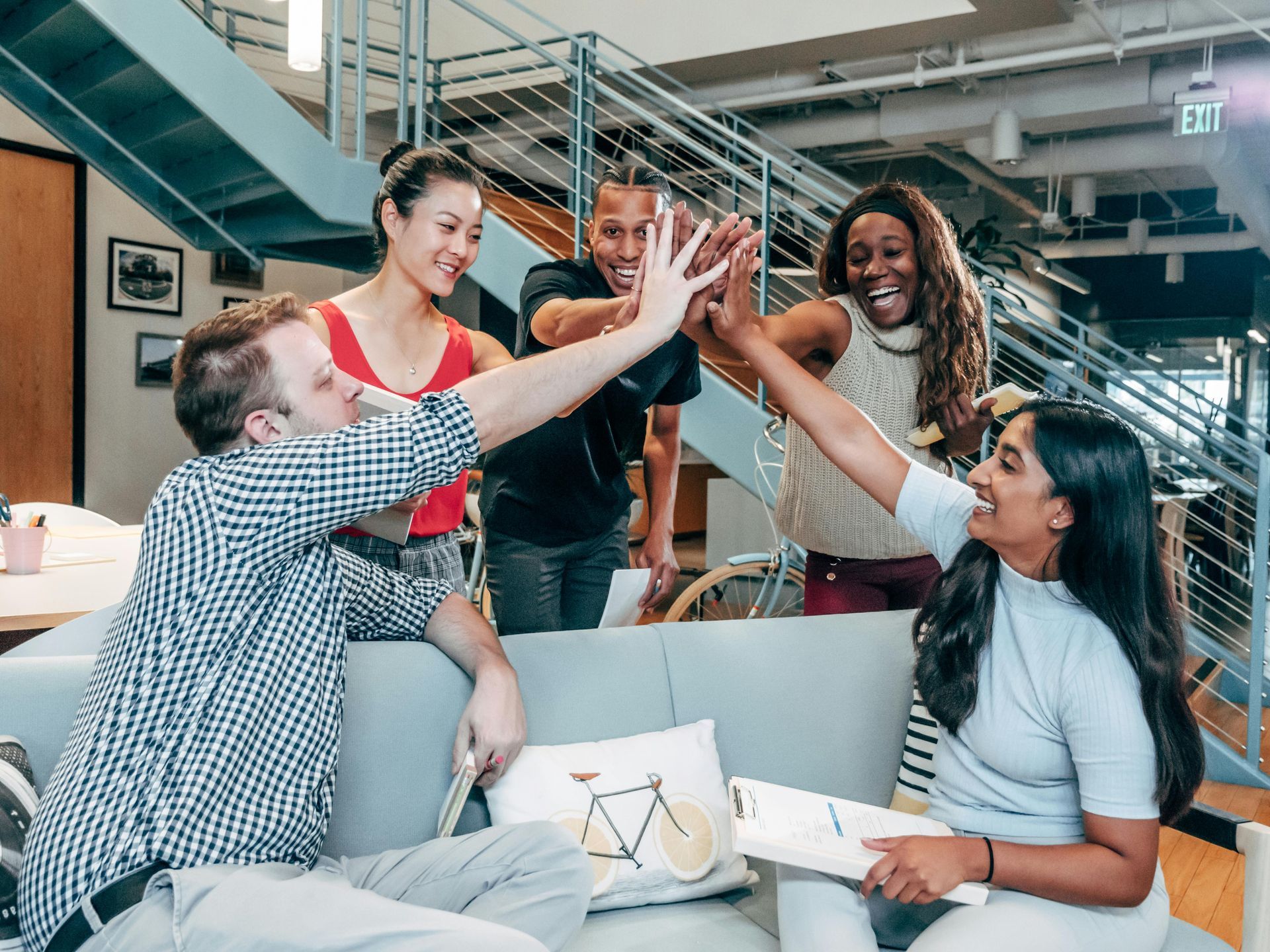 Group of people celebrating, high-fiving. Office setting, smiles, and positive energy are visible.