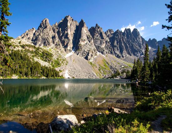 Jagged mountain peaks reflected in a calm alpine lake under a clear blue sky