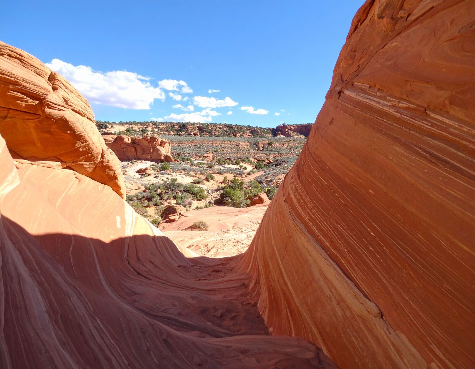 Sandy red sandstone canyon opening to a bright desert landscape under a blue sky
