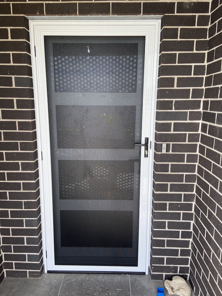 A White Screen Door Is On A Brick Wall — Browny's Glass & Aluminium in Wingham, NSW