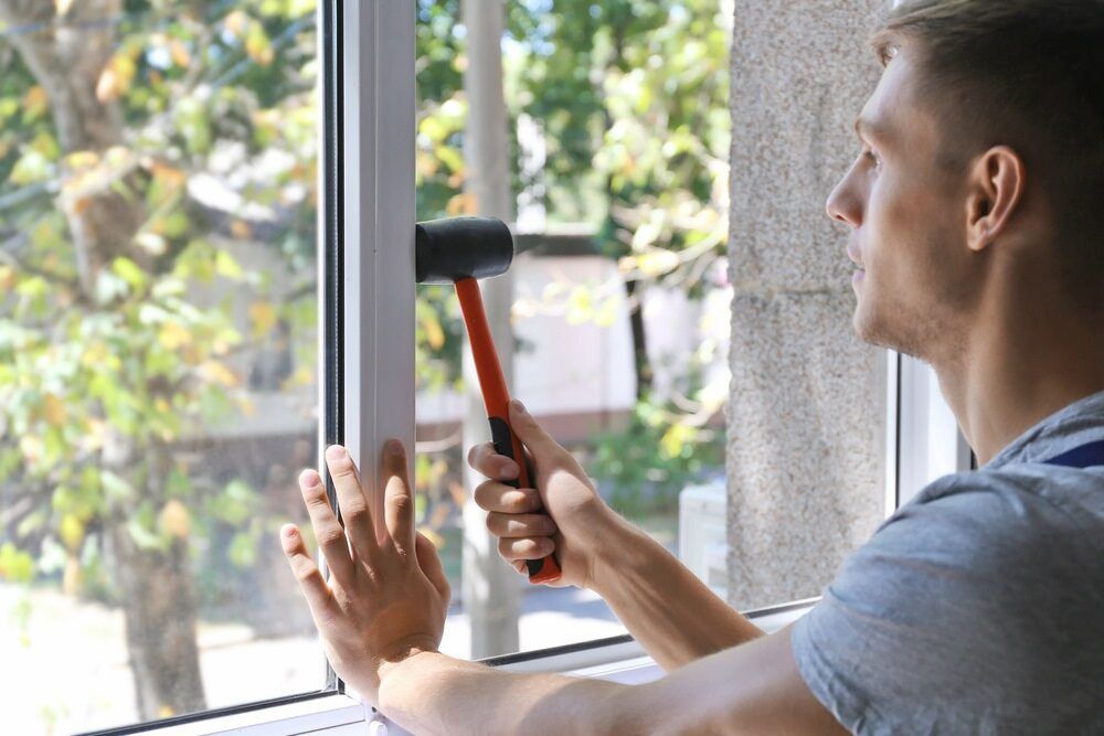 A Man Is Using A Hammer To Fix A Window — Browny's Glass & Aluminium in Wingham, NSW