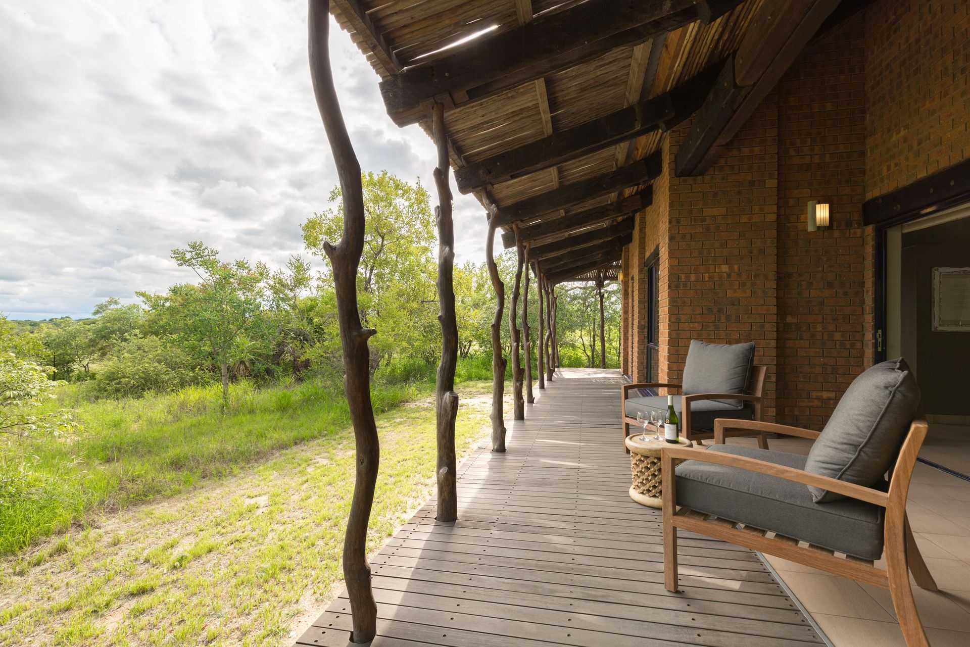 Covered wooden porch with chairs overlooking a green field under a cloudy sky