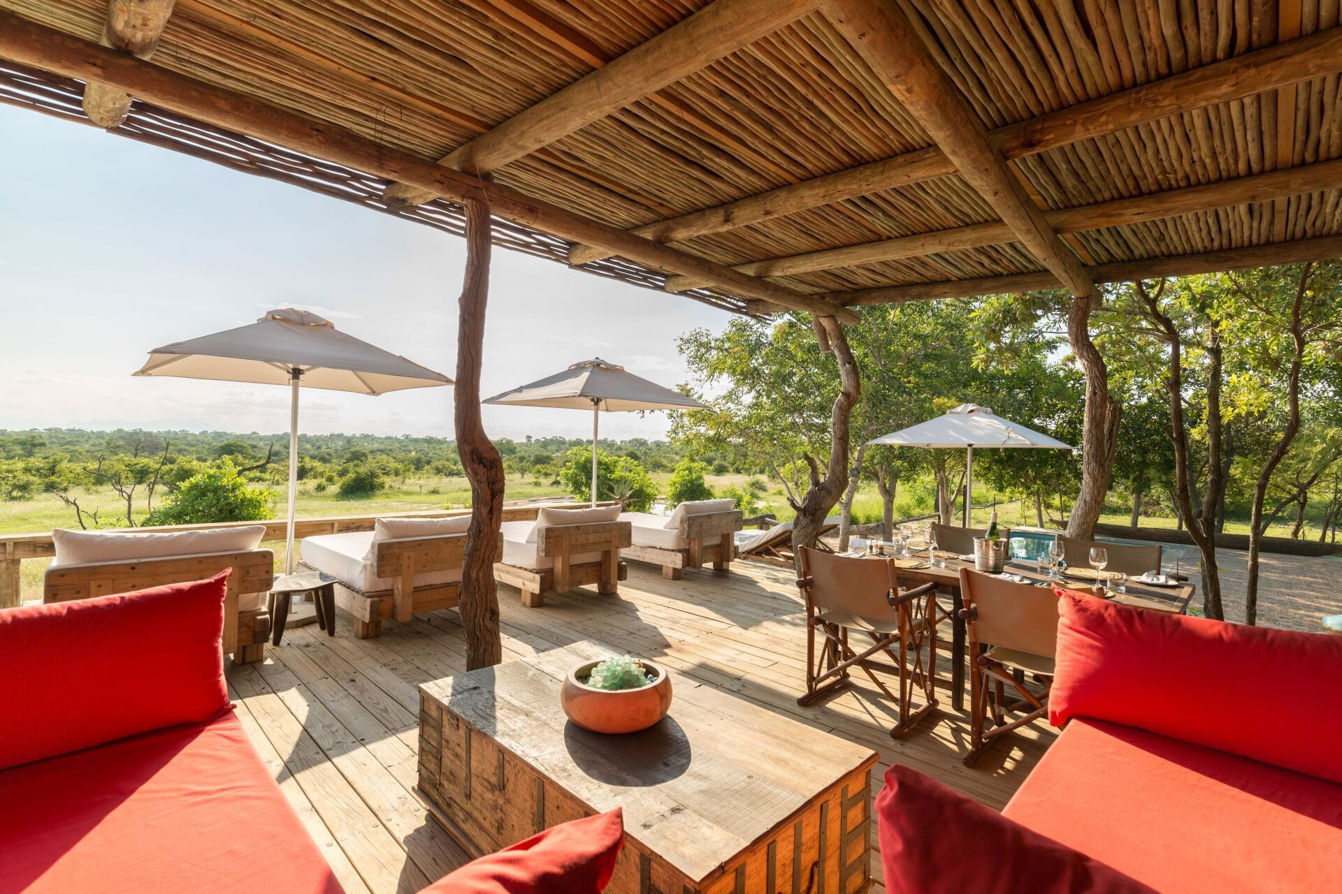 Covered patio lounge with red seating, wooden furniture, and white umbrellas overlooking a green landscape
