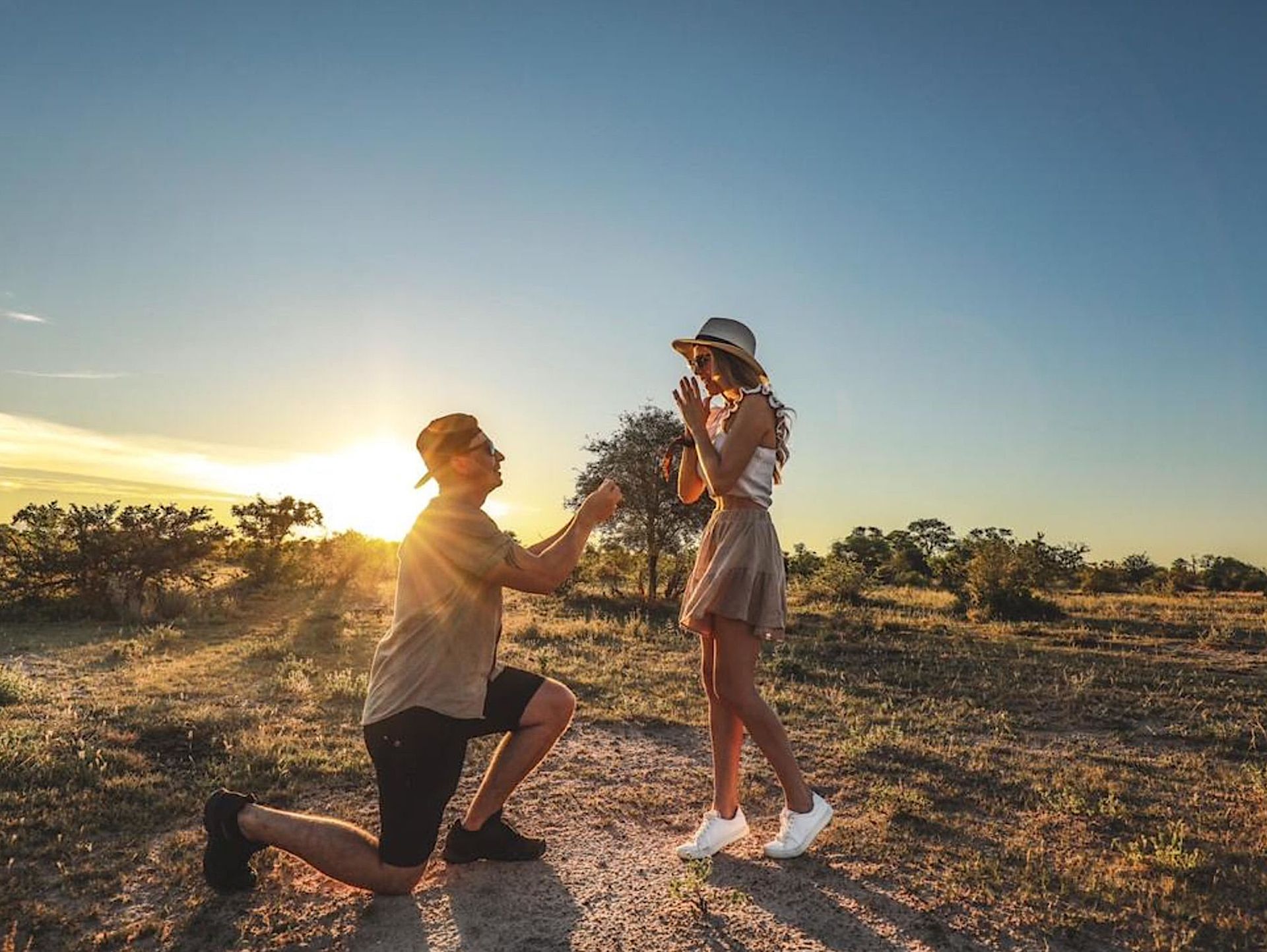 Person kneeling and offering flowers to another person in a sunlit field at sunset