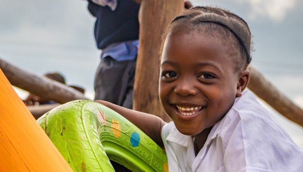Smiling child leaning on a bright green drum outdoors at a playful gathering