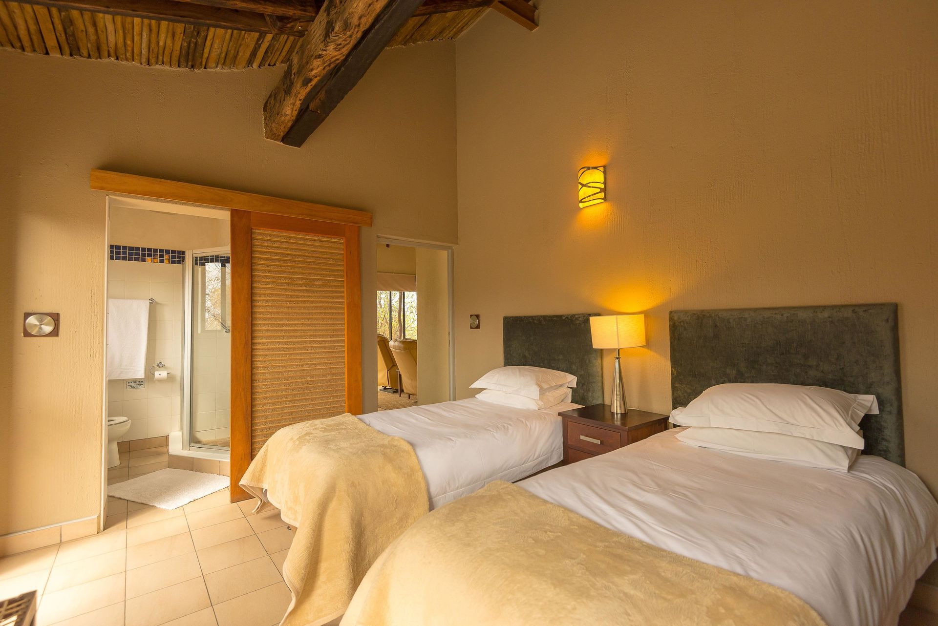 Warm hotel room with two twin beds, bedside lamp, and open doorway to a bathroom