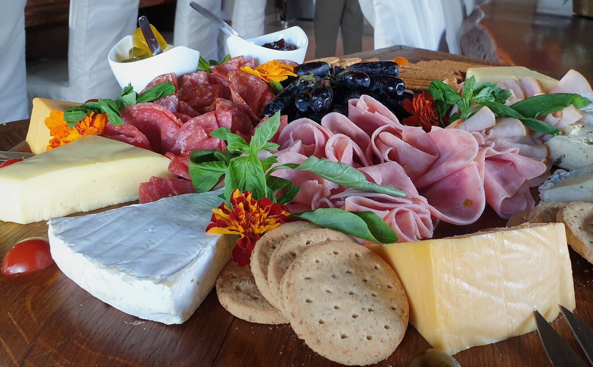 Cheese and cured meat platter with bread, grapes, and herbs on a wooden board