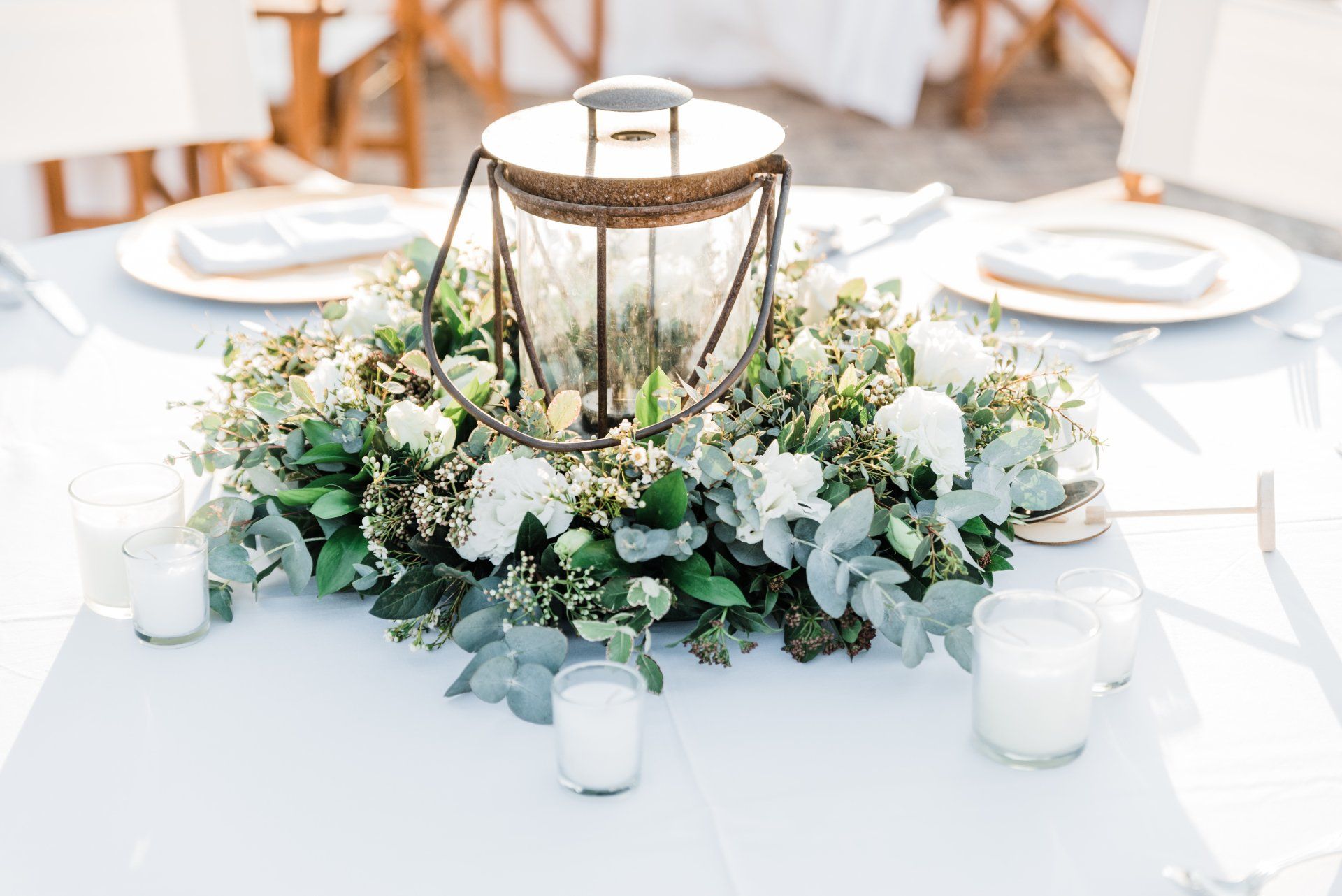 White floral centerpiece with a brass lantern on a set dining table at an elegant event
