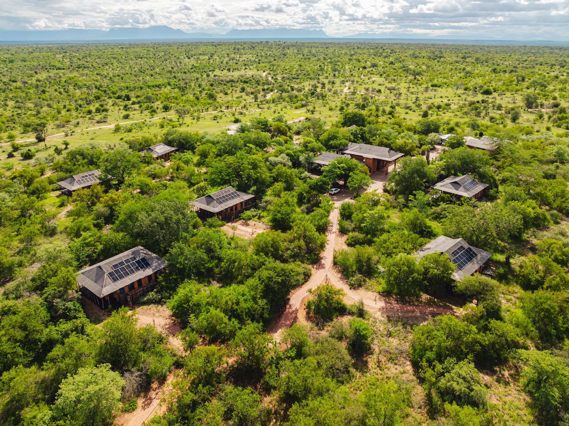 Aerial view of small huts scattered among dense green savanna trees under a wide sky.