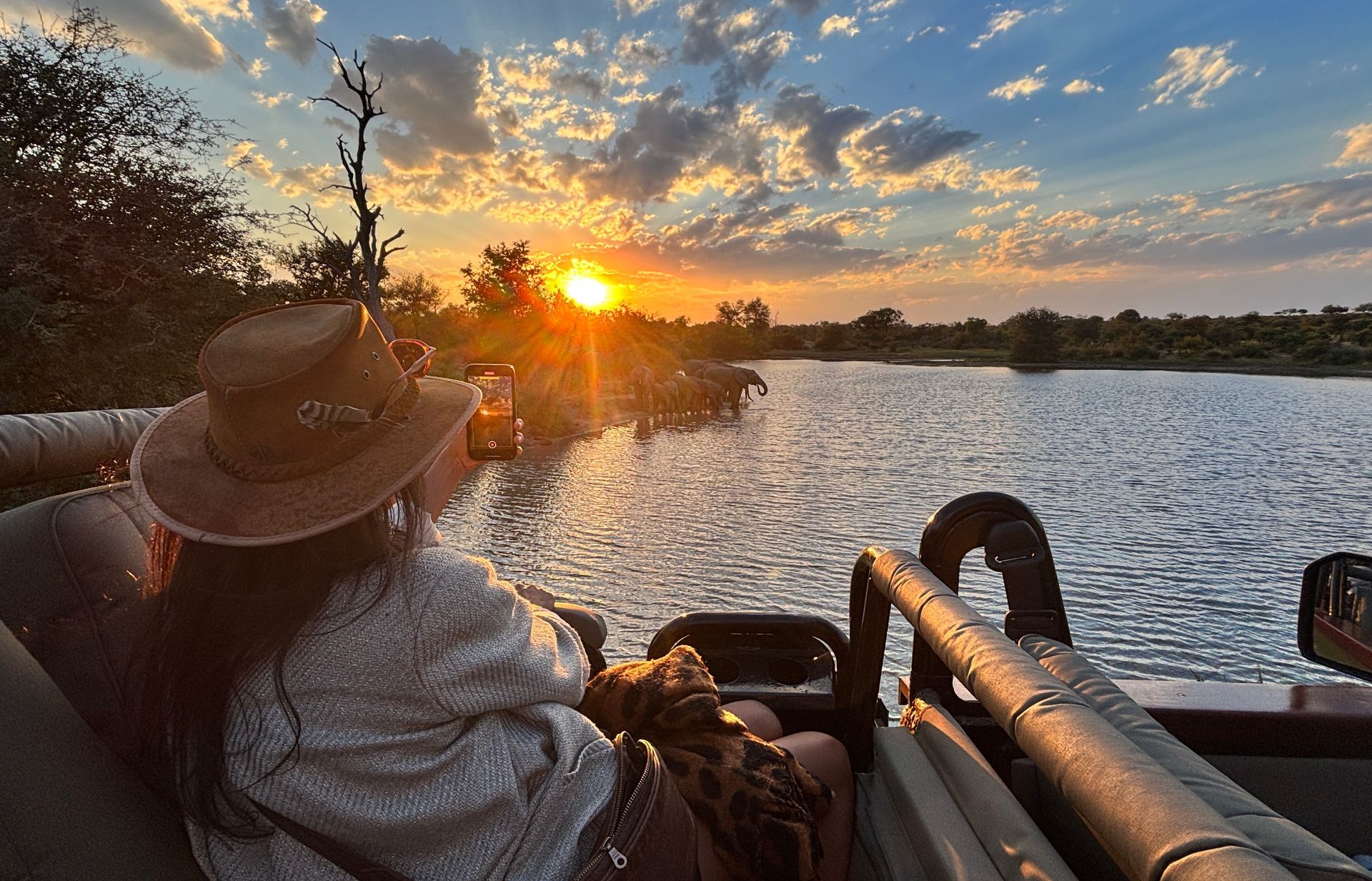 Person in a hat relaxing by a lake at sunset, with golden light reflecting on the water.