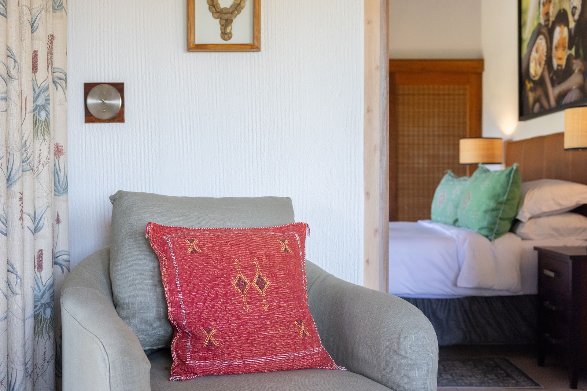 Cozy bedroom with gray armchair, red pillow, and bed with green accent pillows in the background