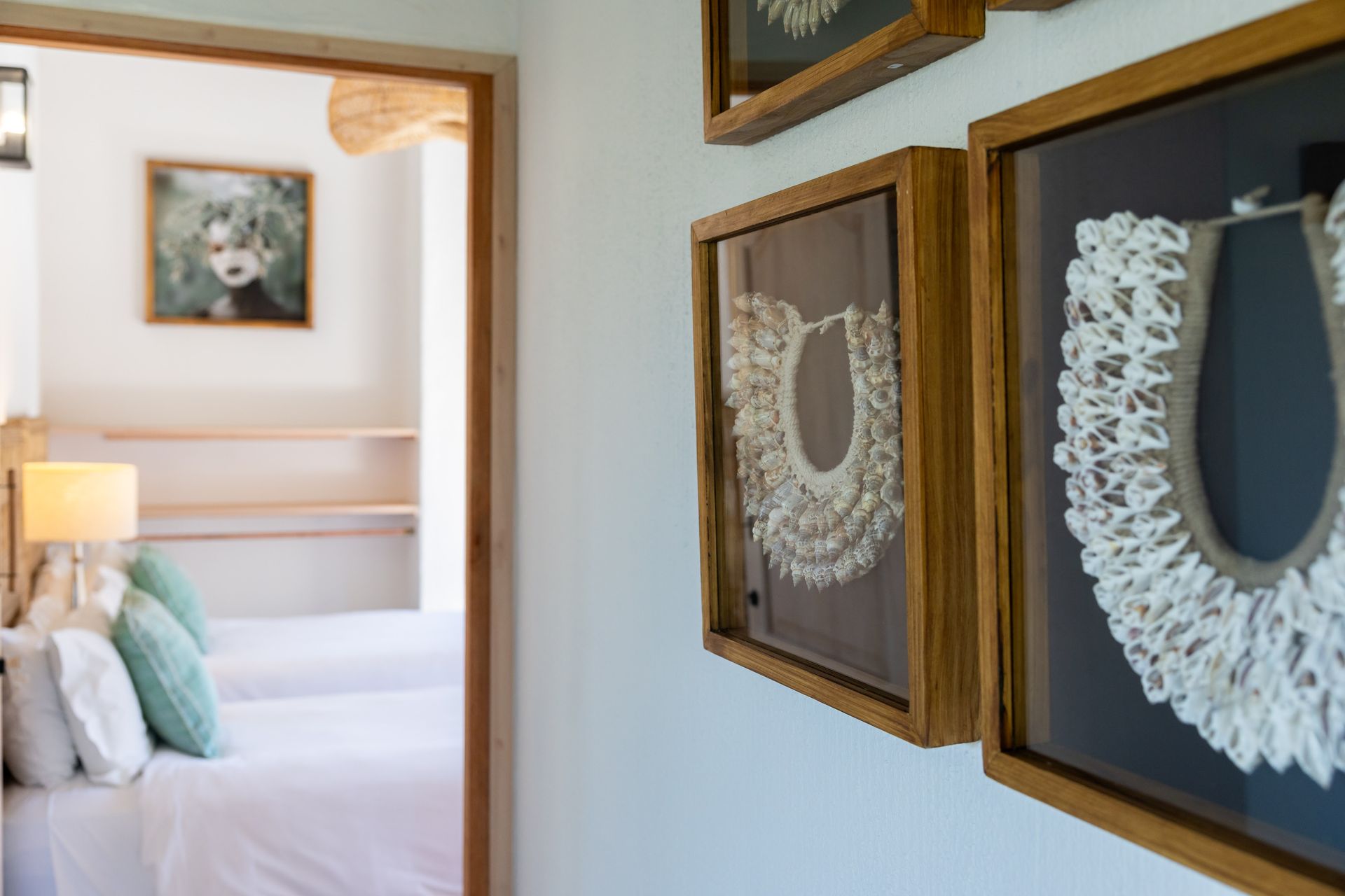 Hallway wall with framed lace art beside a bedroom with a white bed and teal pillows
