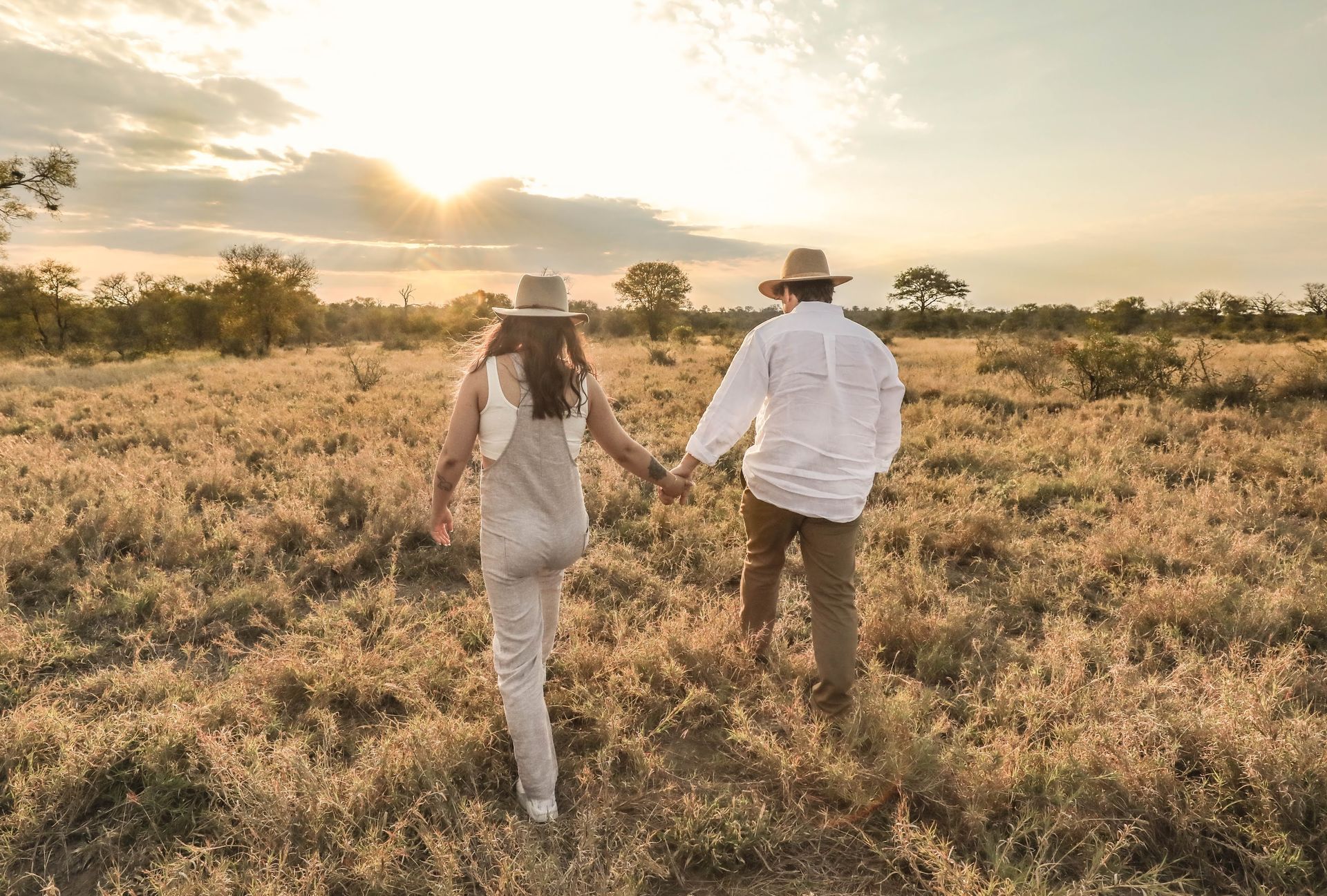 Couple holding hands walking through a sunlit grassy field at sunset