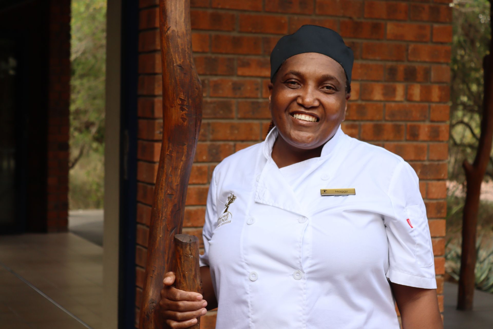 Smiling hotel staff member in a white uniform standing by a brick wall and doorway