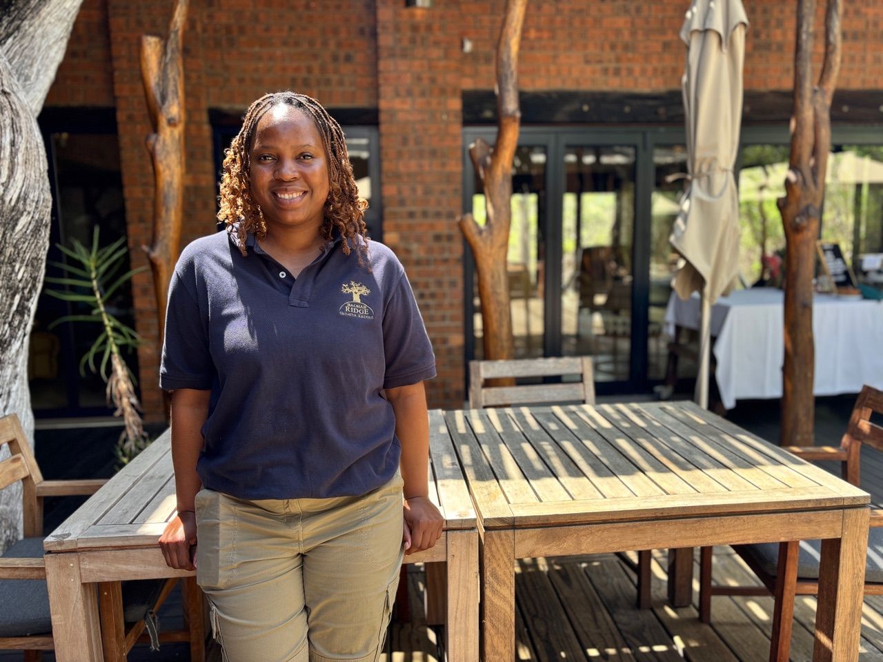 Person standing on a wooden deck beside patio tables in front of a brick building.
