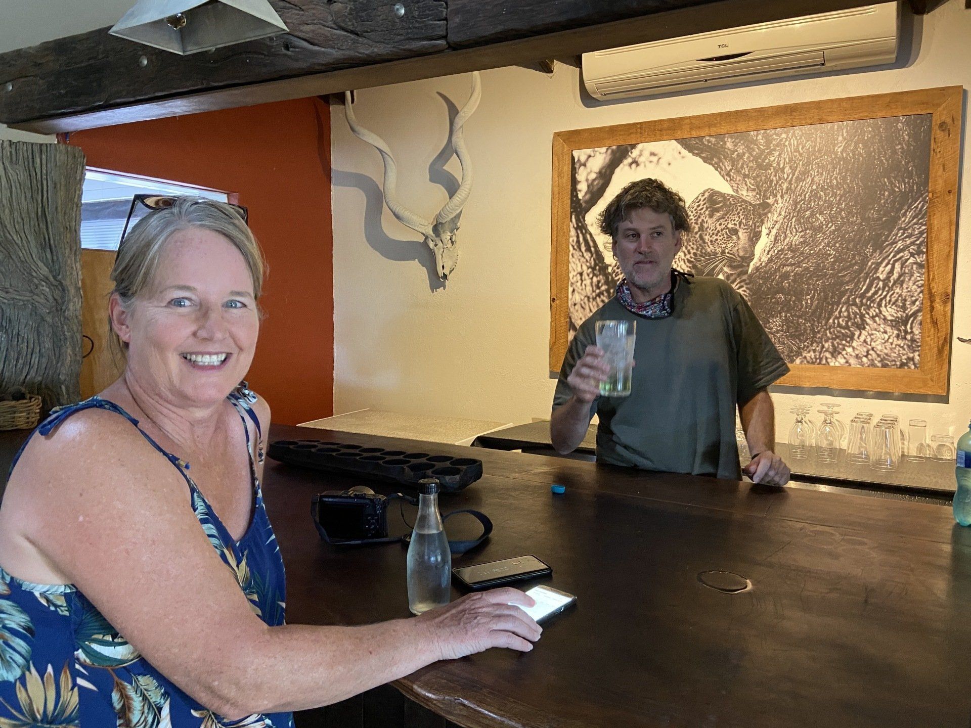 Two people at a wooden bar in a rustic indoor space, one smiling and holding a drink