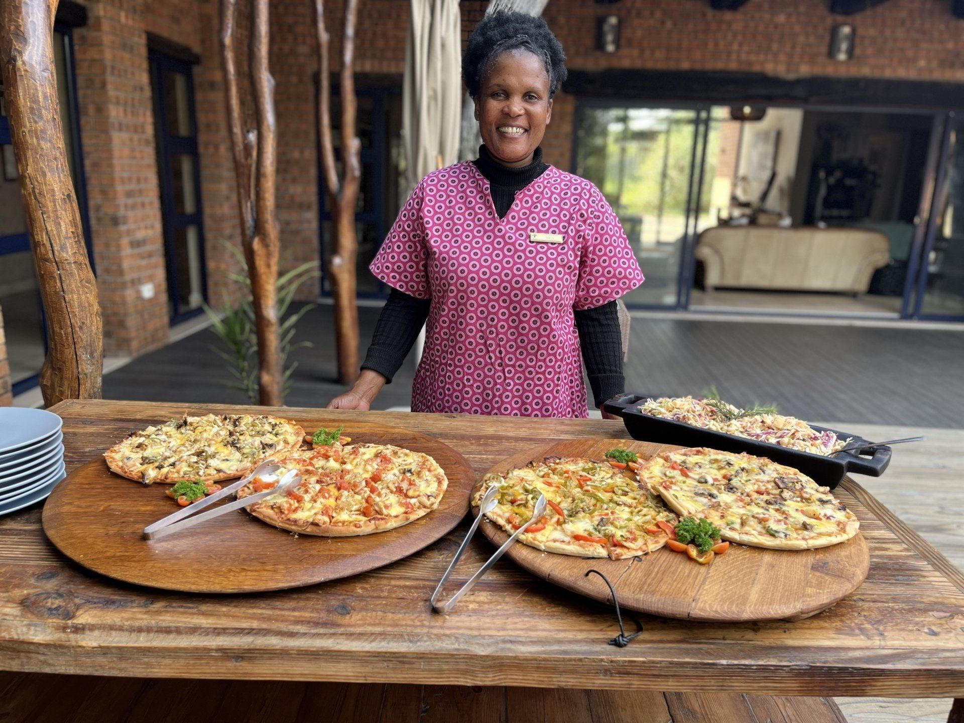 Person smiling behind table of pizzas in a kitchen patio setting