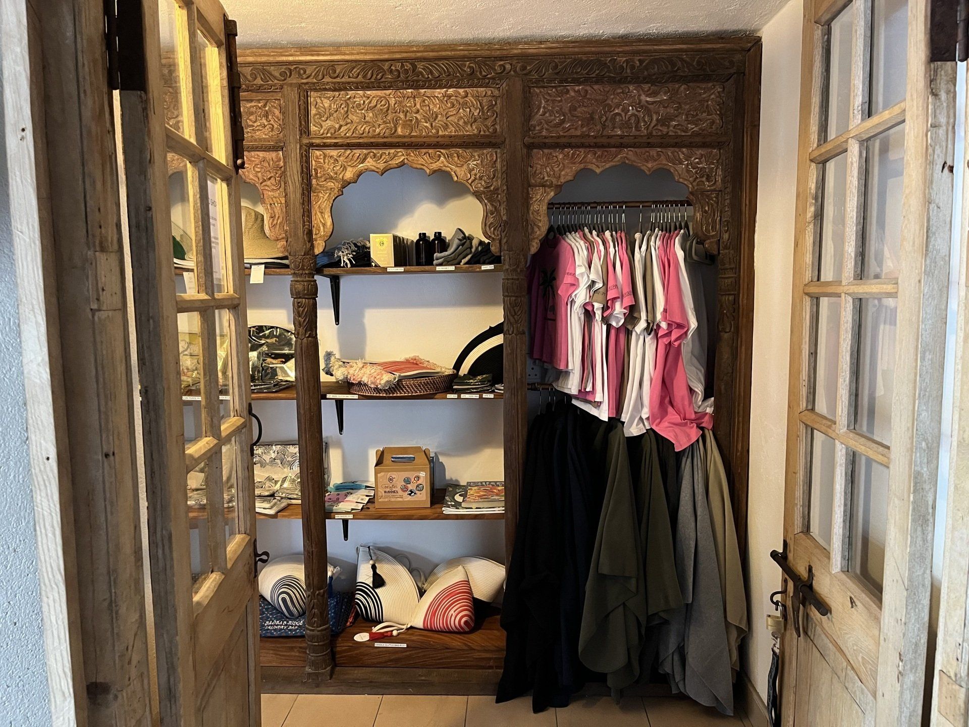Closet with shelves of folded items and hanging pink and black clothes in a rustic room