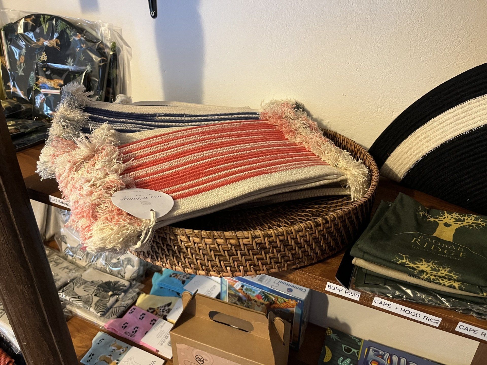 Assorted household items on a shelf, including a wicker tray with folded red-and-white textiles and stacked books.