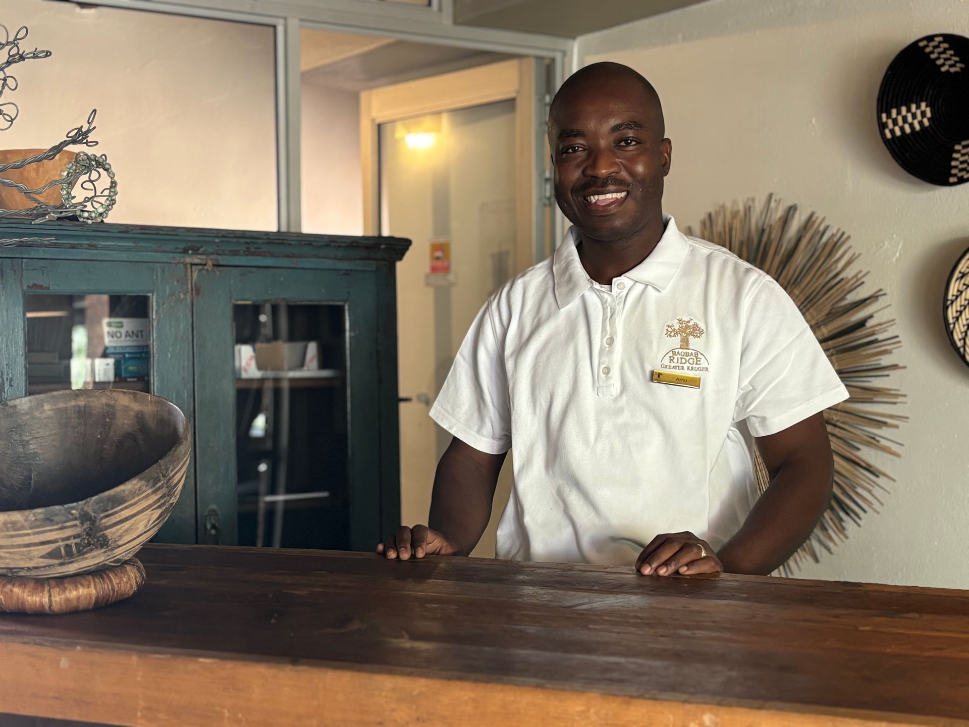 Smiling man in white shirt standing behind a wooden reception desk in a lobby