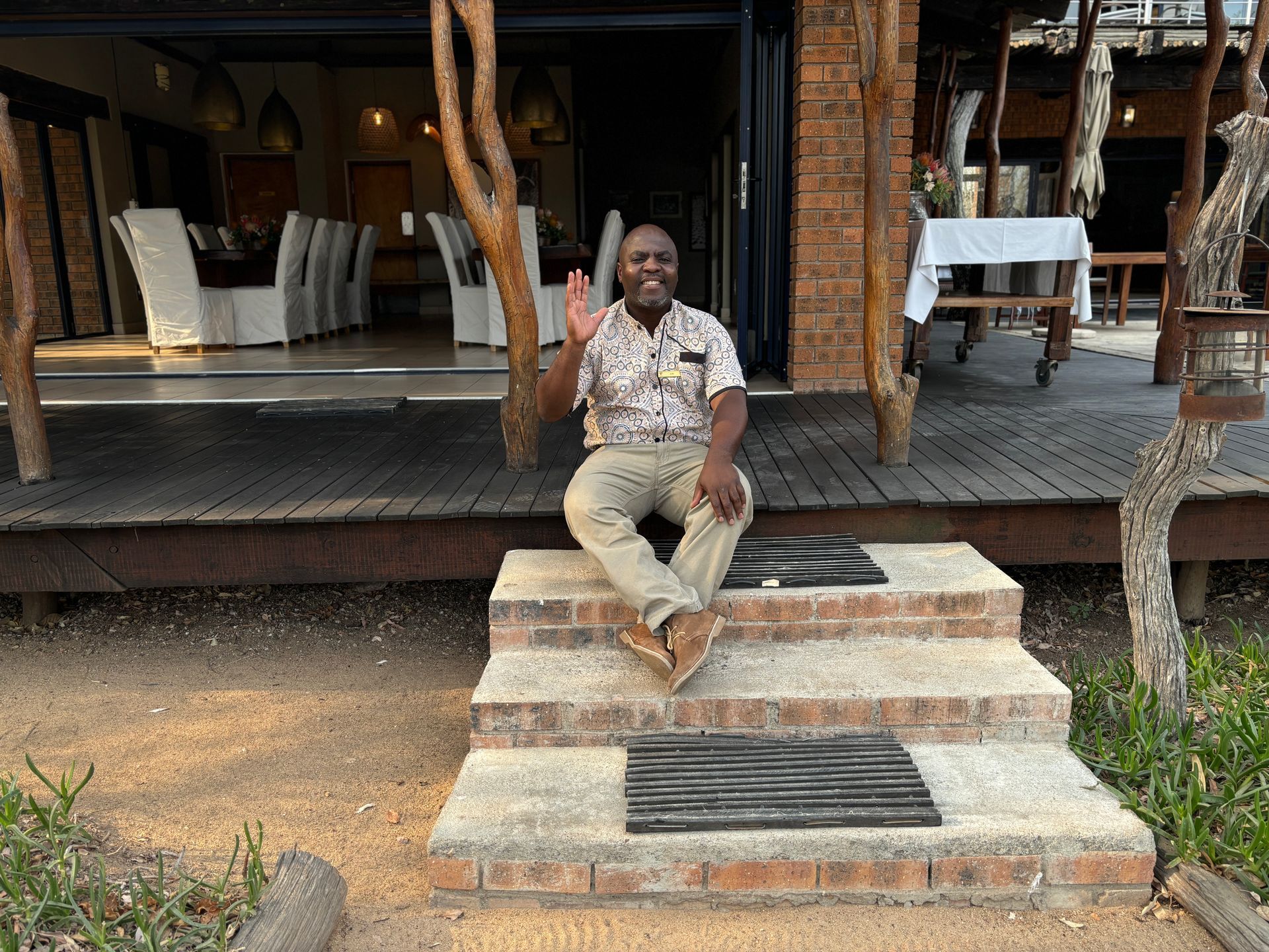Person sitting on stone steps and waving in front of a rustic lodge porch