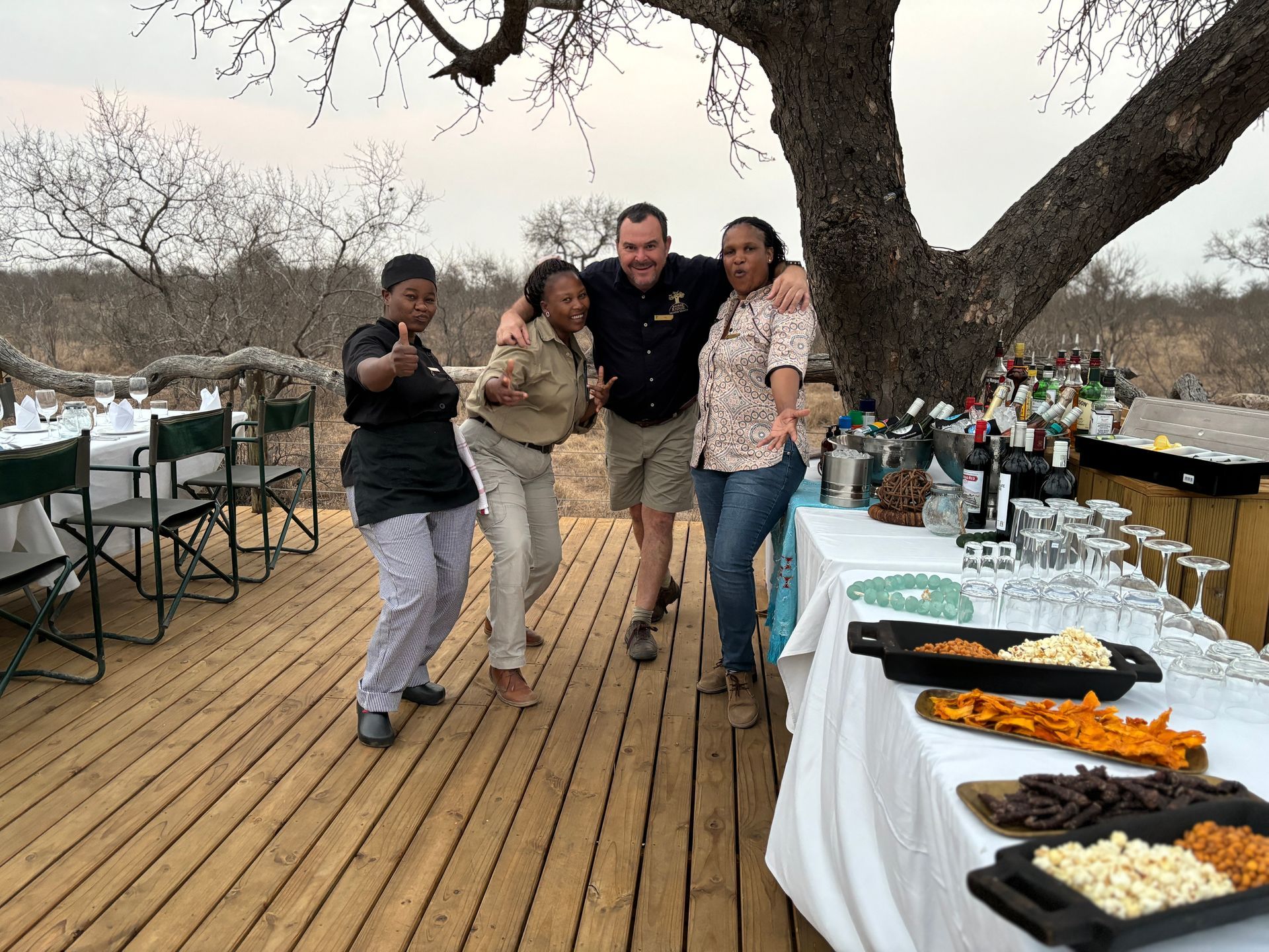 Four people posing on a wooden deck beside a buffet table at an outdoor gathering