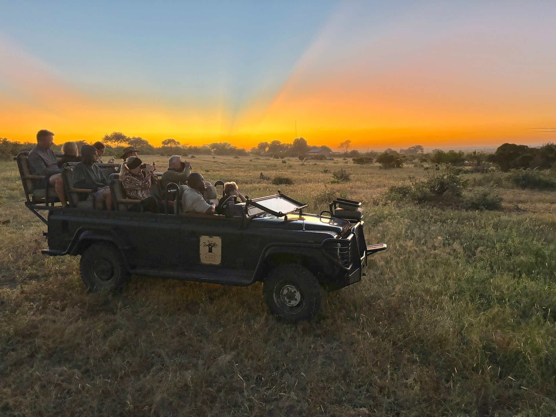Safari jeep with passengers on grassland at sunset