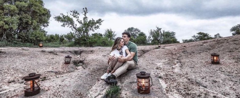 Two people sitting on a rocky hillside with lanterns, under a cloudy sky