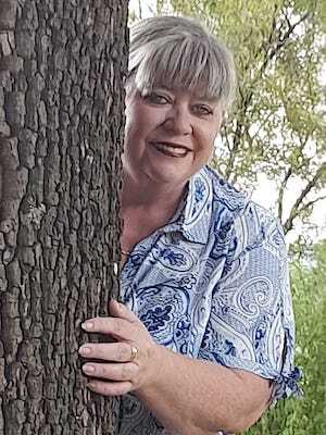 Smiling woman peeks from behind a tree, wearing a blue-and-white patterned shirt.
