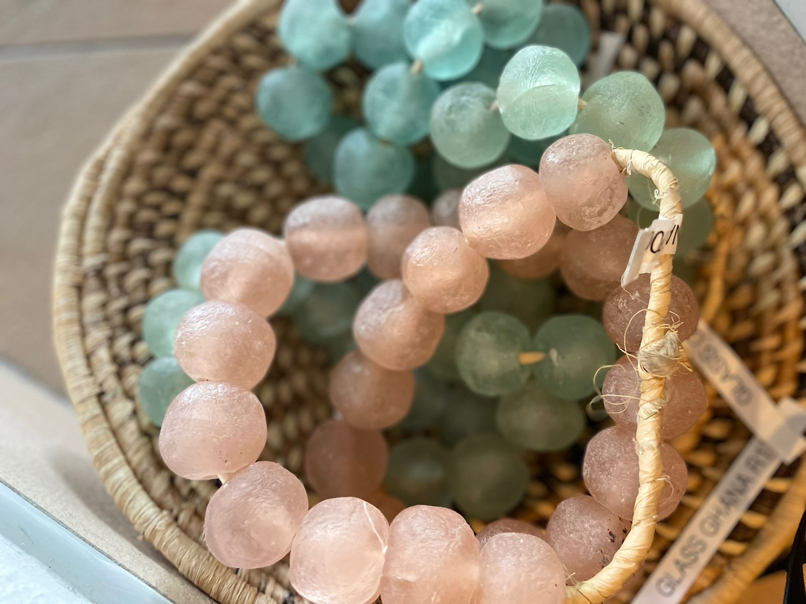 Pastel beaded bracelets in pink, green, and blue stacked in a woven basket