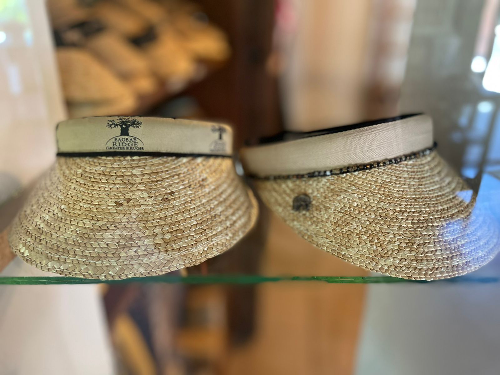 Two woven straw hats with dark bands displayed side by side on a glass shelf