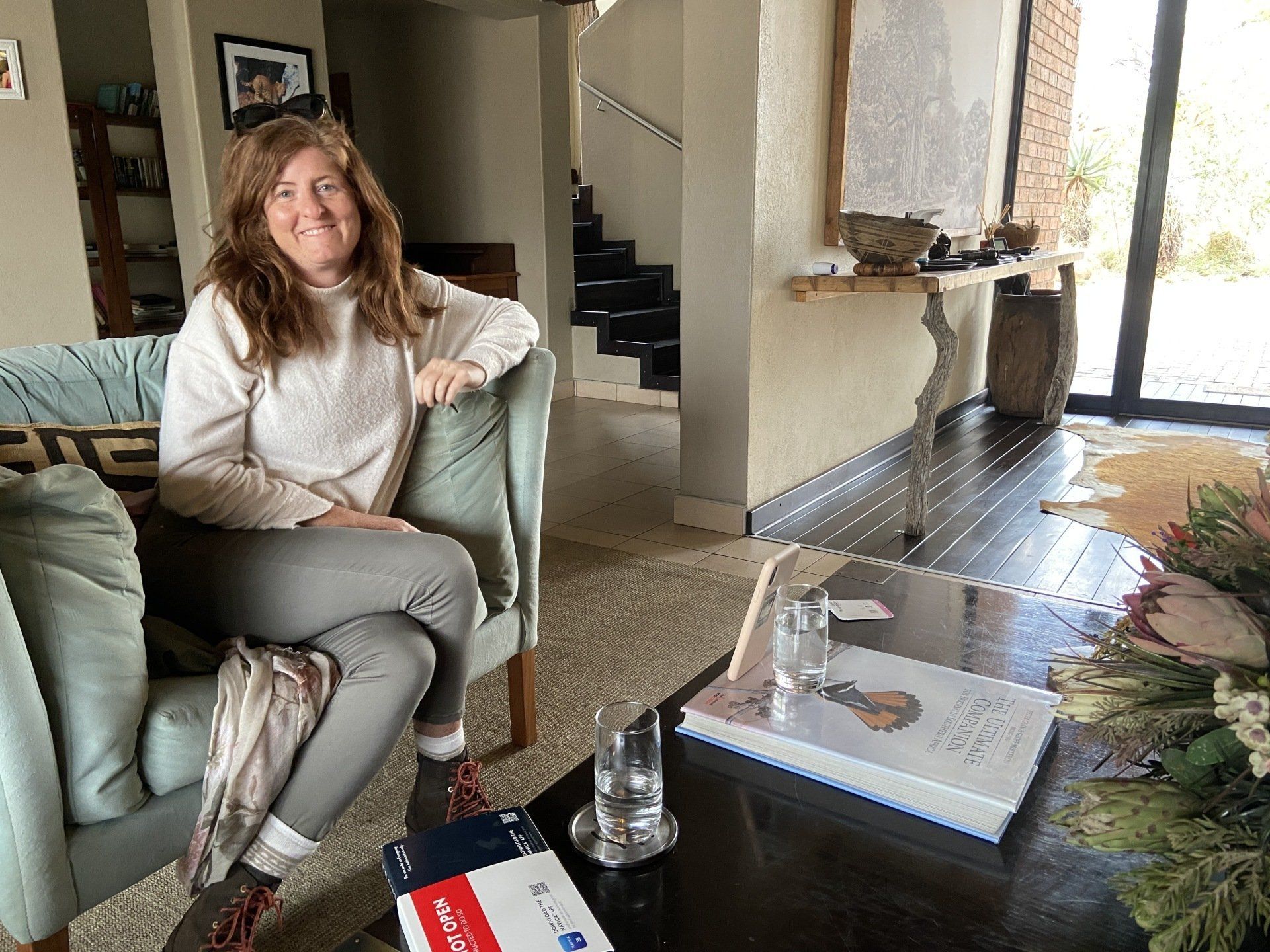 Woman sitting on a green sofa in a bright living room beside a coffee table and fireplace