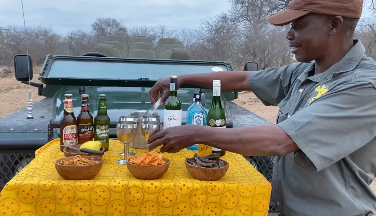 Man arranging drinks and snacks on a yellow table beside a pickup truck outdoors