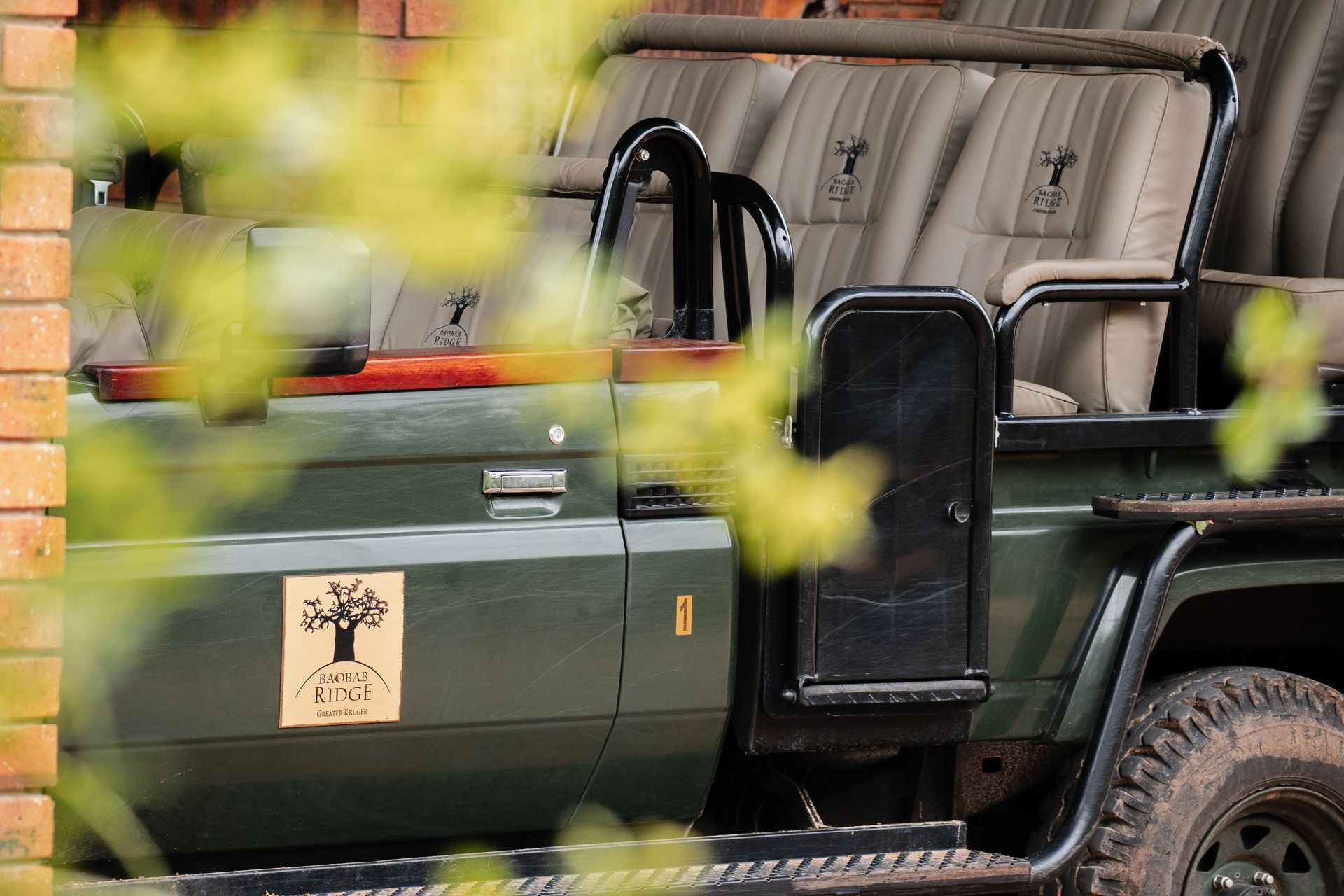 Green safari jeep parked behind blurred leaves and brick wall