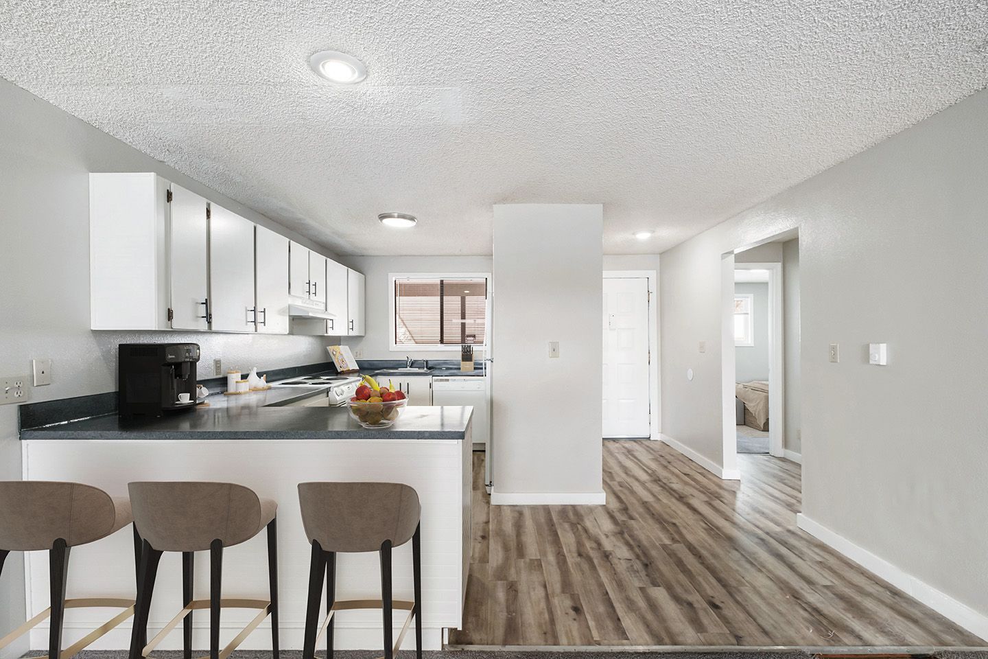 Bright modern kitchen and living area with white cabinets, wood flooring, and bar stools