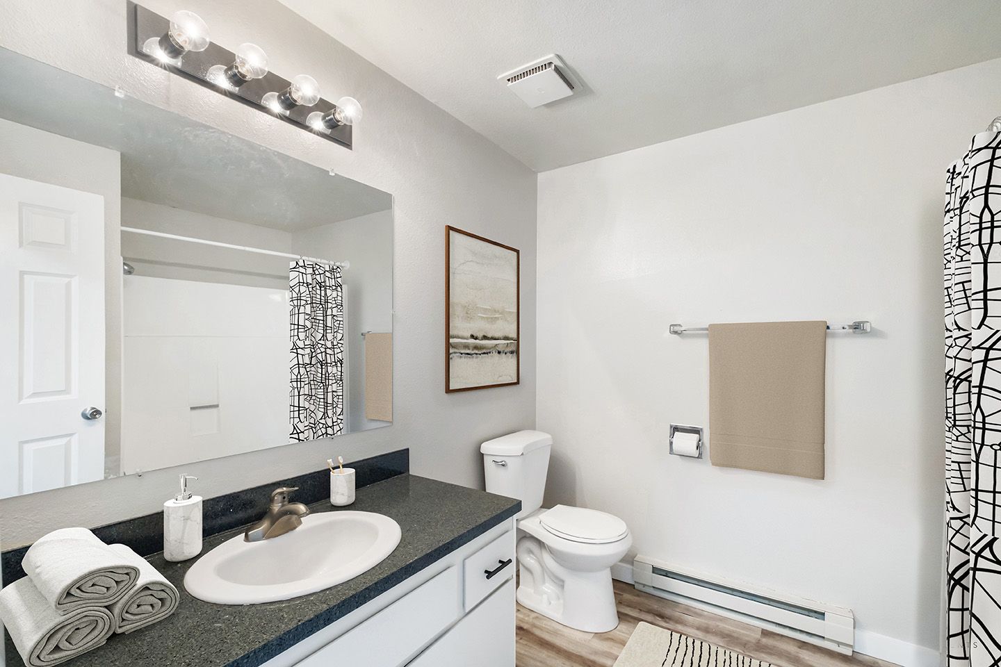 Modern bathroom with white walls, black vanity, large mirror, toilet, towel rack, and patterned shower curtain