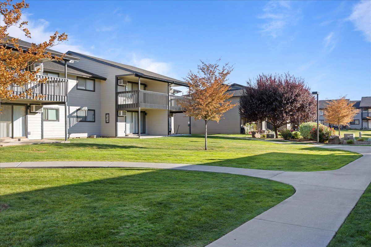 Apartment complex with green lawn, curved sidewalk, and autumn trees on a sunny day