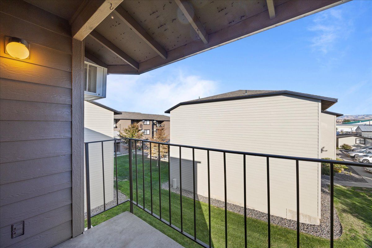 Balcony with black railing overlooking a grassy courtyard and beige buildings under a blue sky