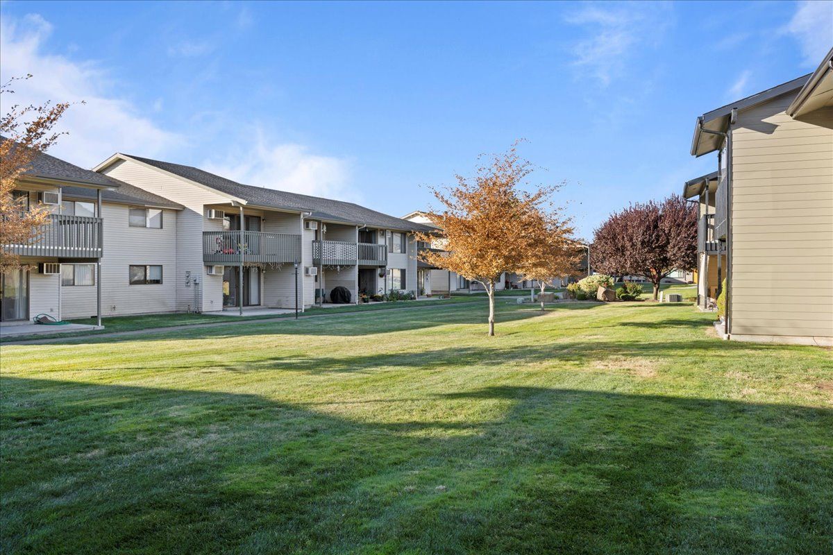Apartment complex courtyard with green lawn, trees, and beige buildings under a blue sky