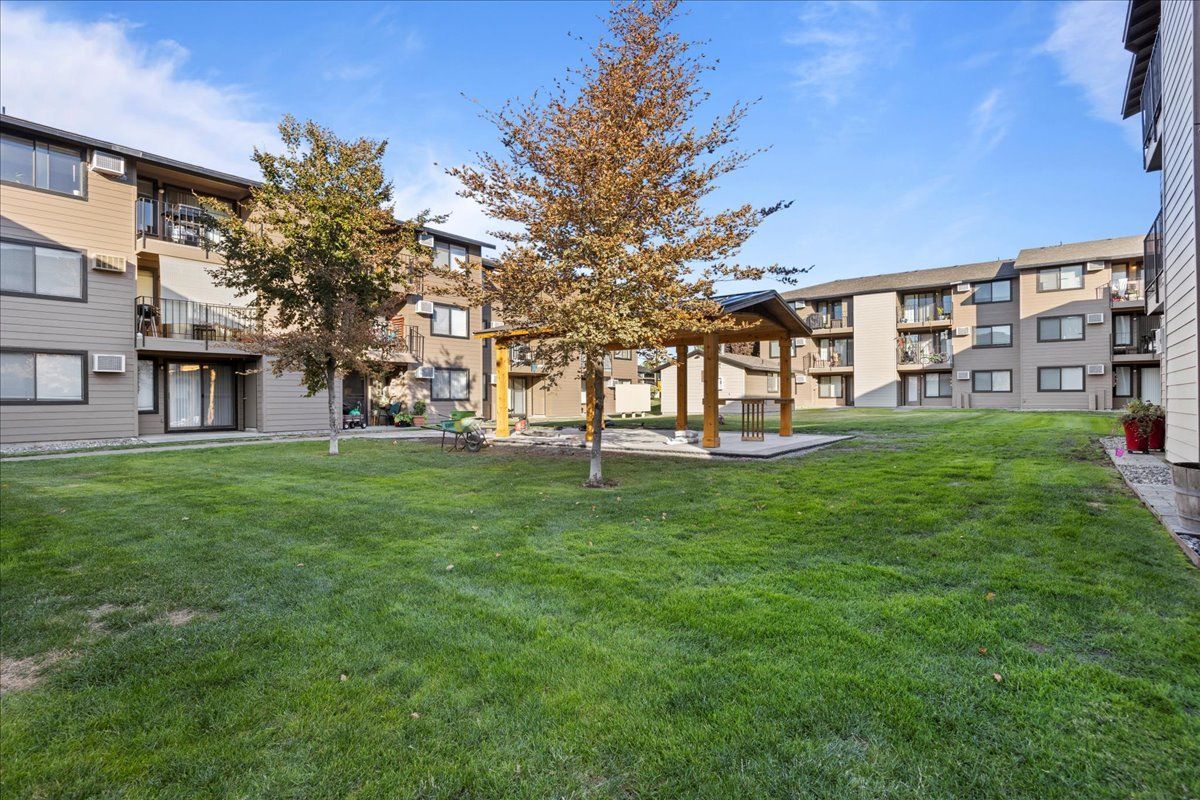 Apartment courtyard with green lawn, trees, and a covered seating area between buildings